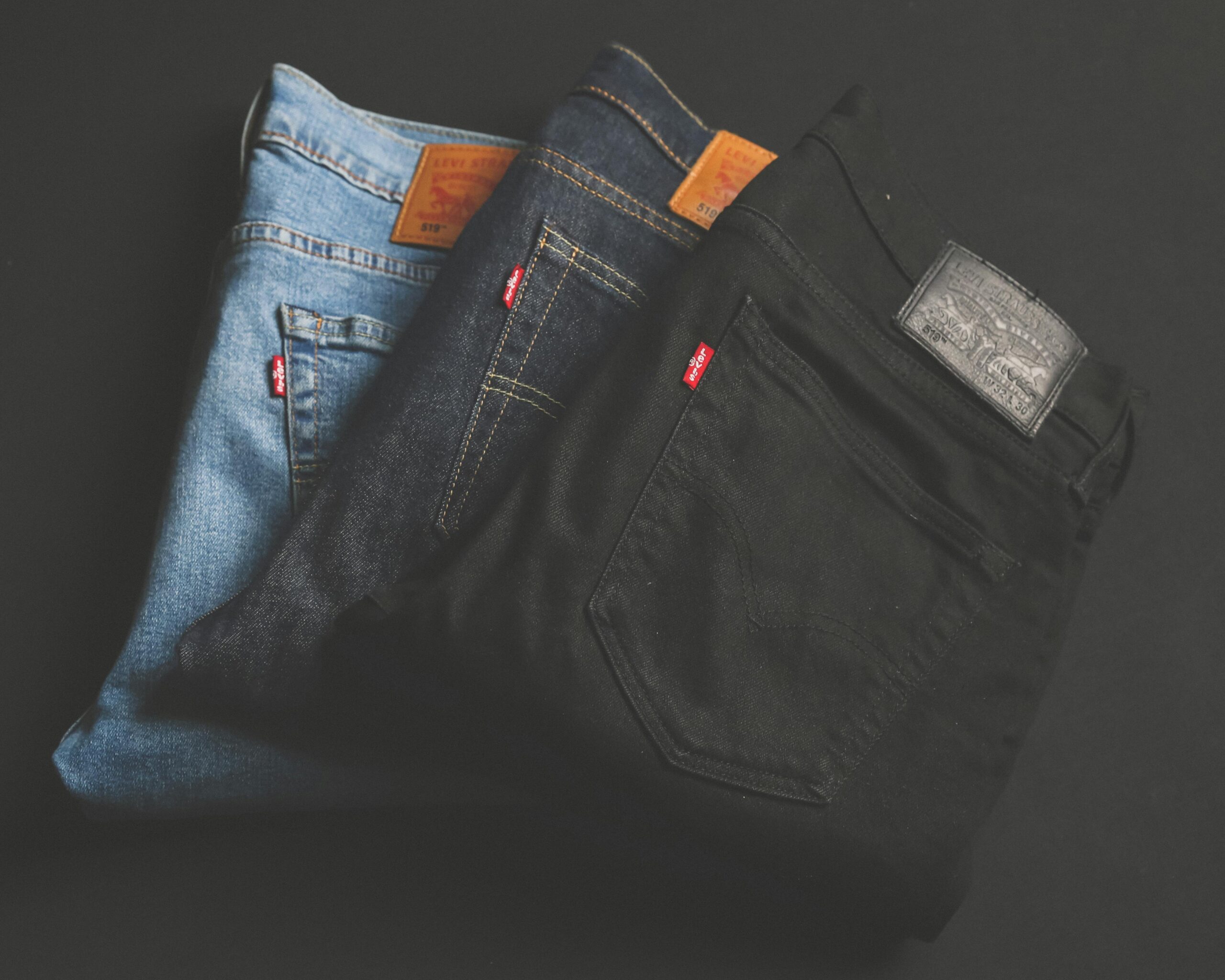 A stack of blue, dark, and black denim jeans folded on a dark surface.