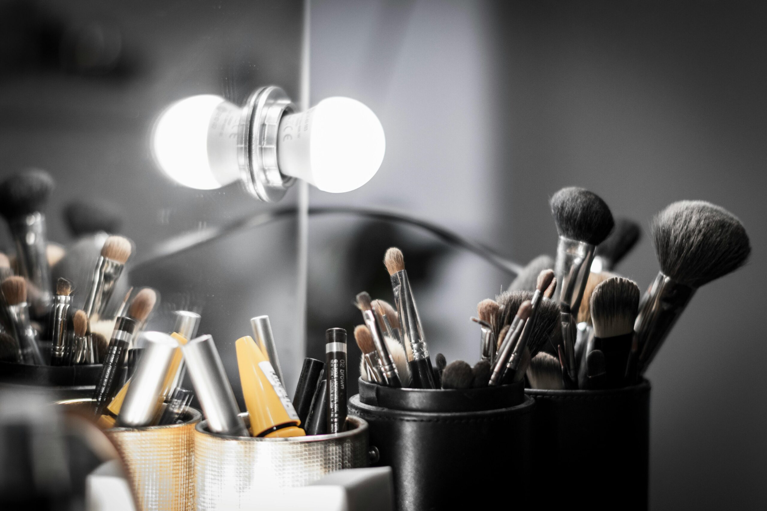 Close-up of makeup brushes and light bulb reflection creating a studio vanity atmosphere.